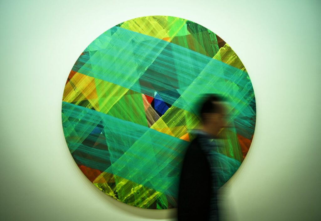 Abstract circular artwork with vivid colors and a blurred human silhouette walking by.