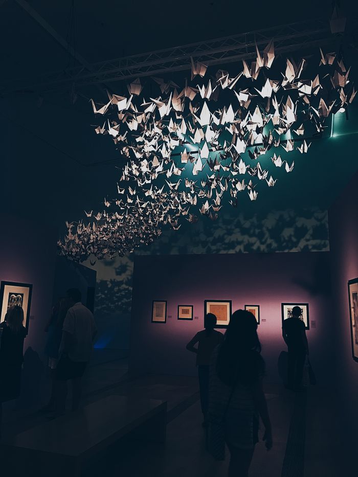 Elegant origami display in a dimly lit Singapore art gallery with a crowd.